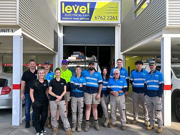 Staff group posing outside a Level Truck Repairs garage with blue signage and a tow truck in the bay — Level Electrical & Air In Tamworth, NSW