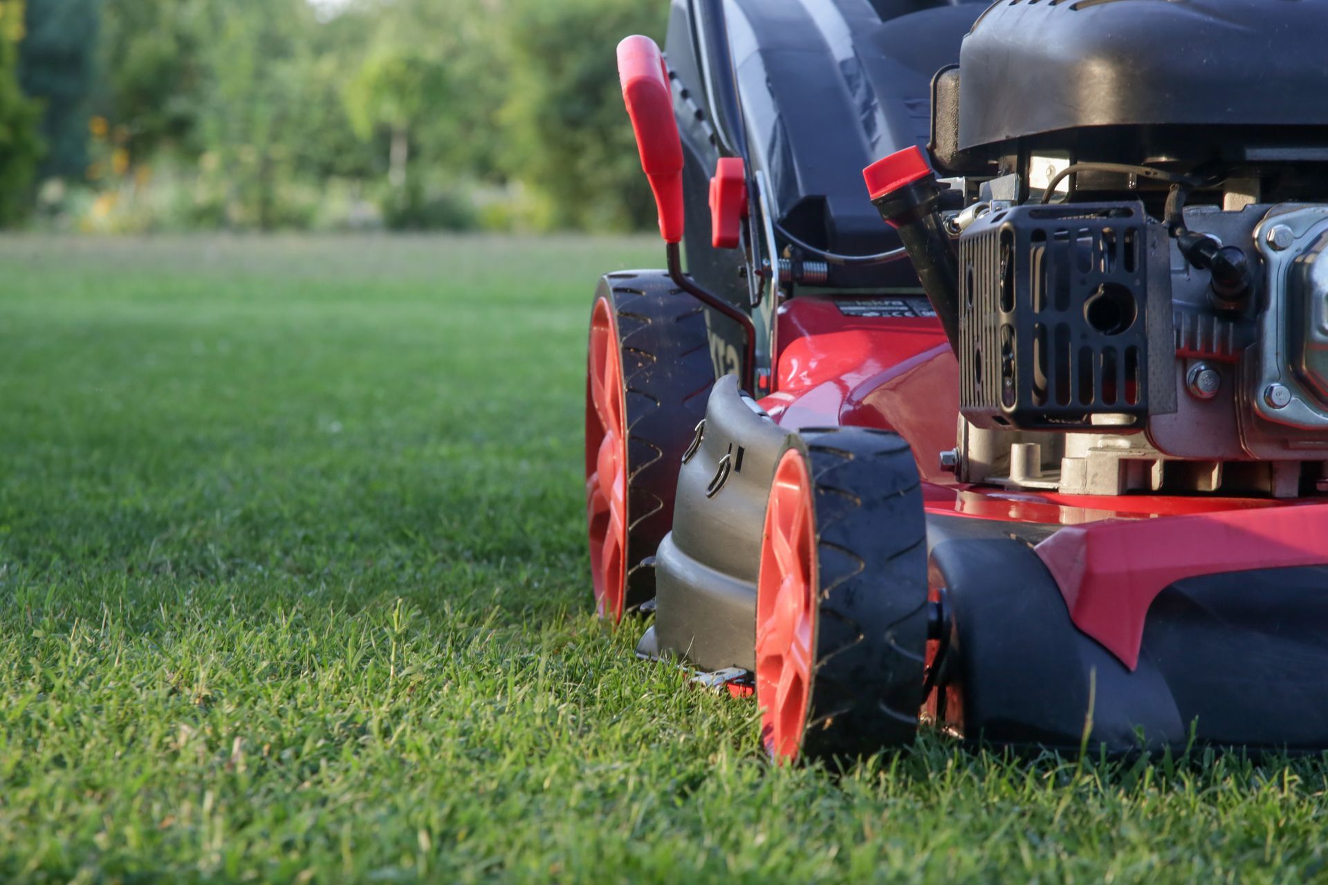 A red lawnmower with bright orange wheels resting on a freshly cut green lawn.