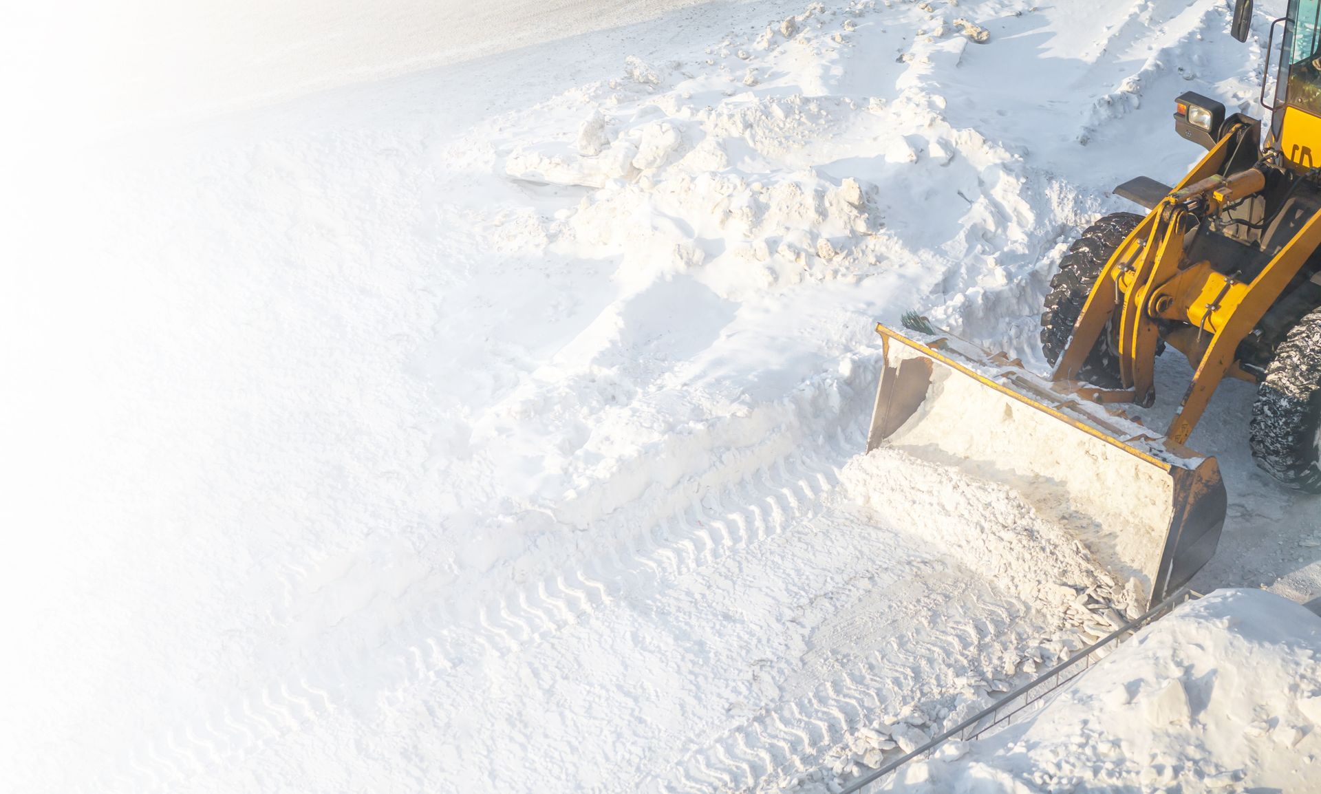 A yellow snowplow clearing white snow from a path.