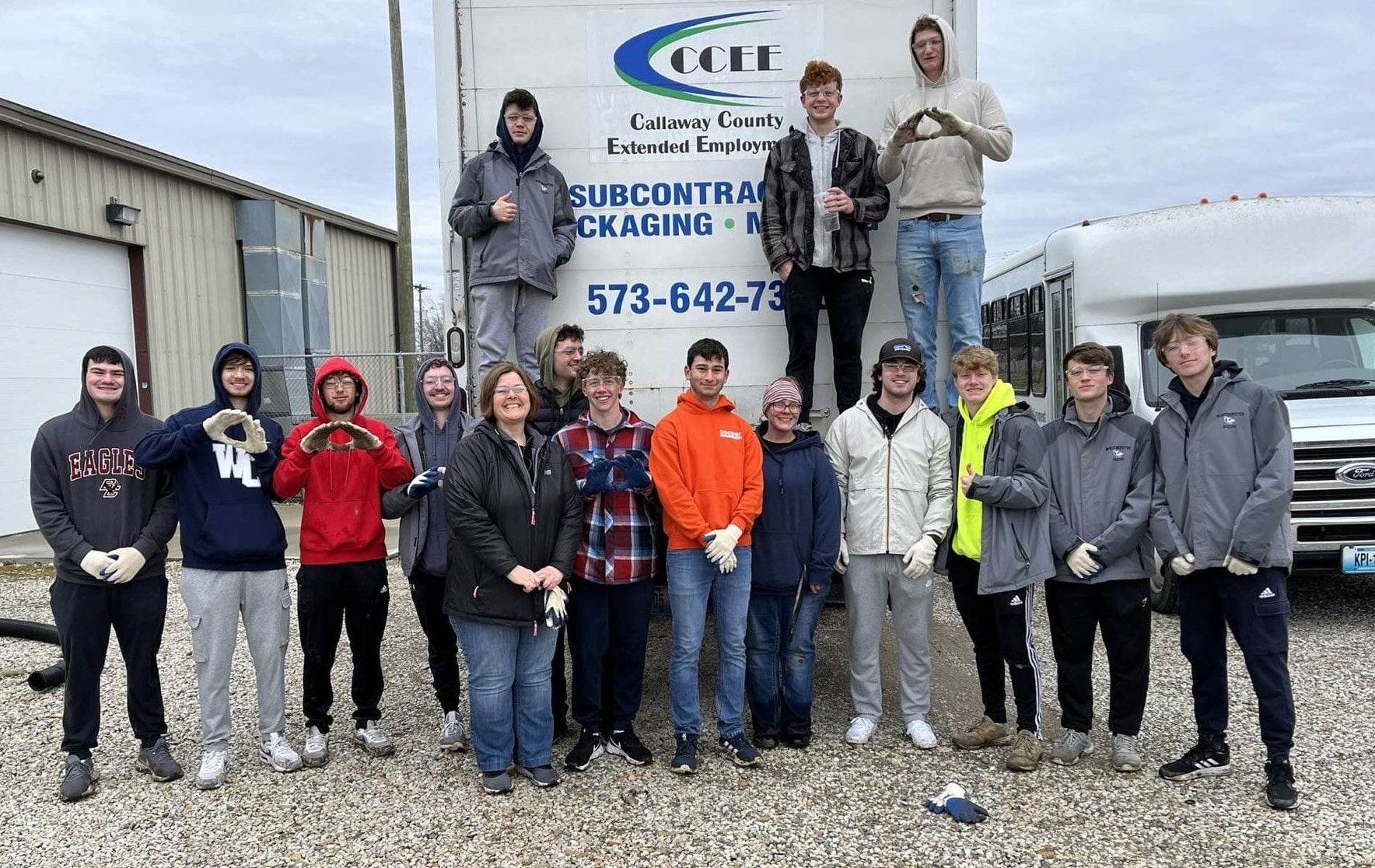 Group of people standing in front of a white truck, likely a work crew, some holding tools.