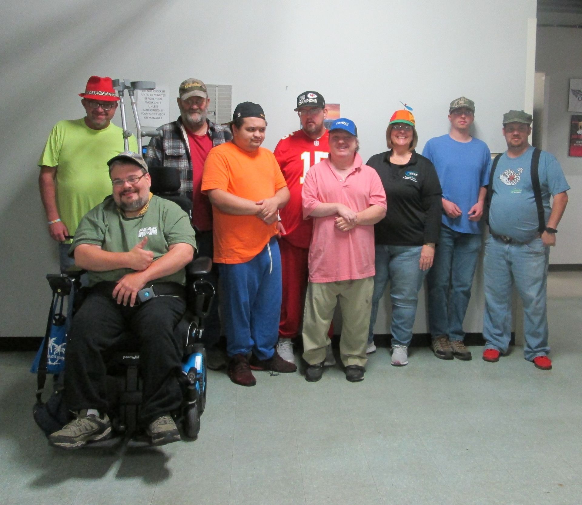 Group of people indoors, some wearing hats, smiling. One person in a wheelchair.