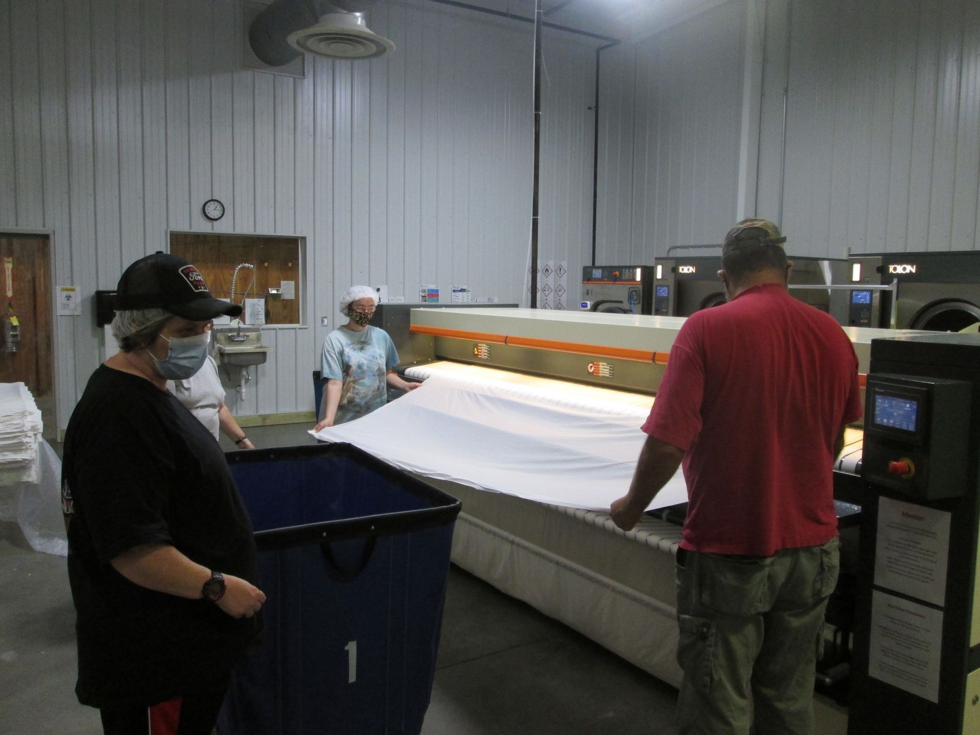 People folding a large white sheet in a laundry facility. People folding a large white sheet in a laundry facility.