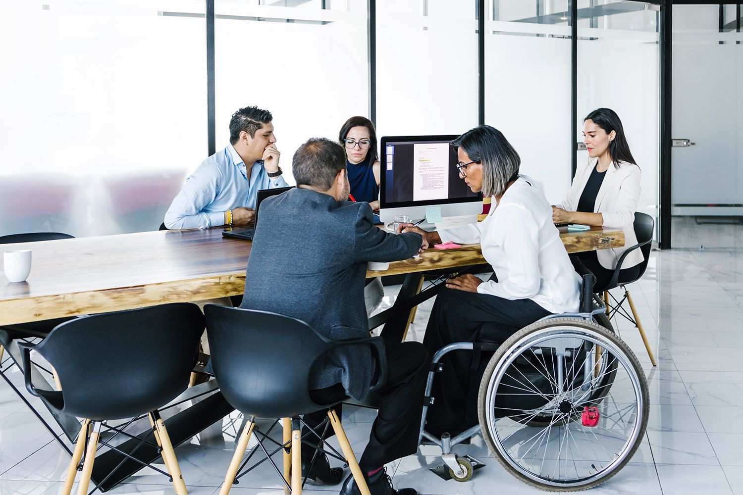 Group of people in an office meeting around a table, reviewing documents and a computer screen. Group of people in an office meeting around a table, reviewing documents and a computer screen.