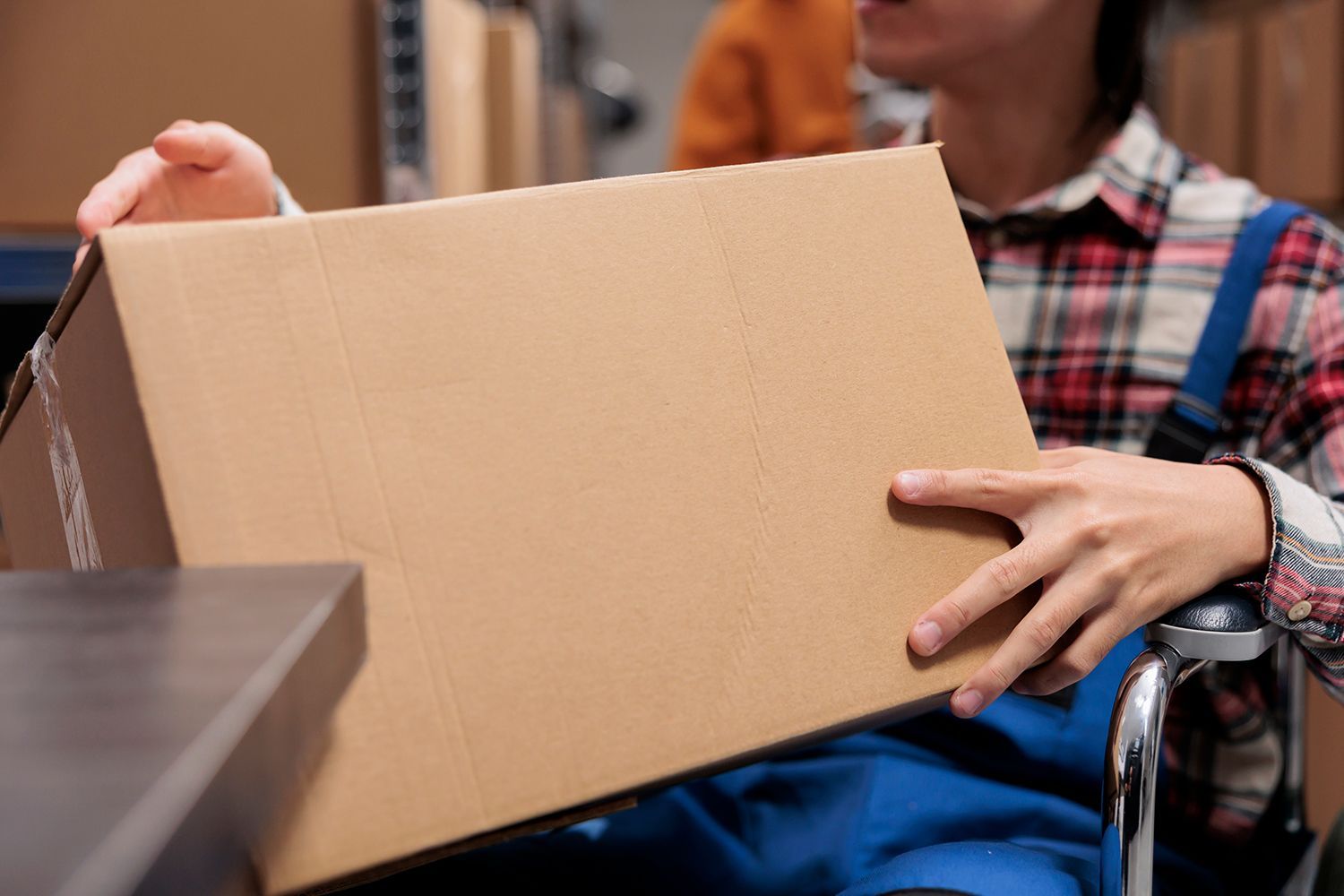 Person in a wheelchair holding a cardboard box in a warehouse. Person in a wheelchair holding a cardboard box in a warehouse.