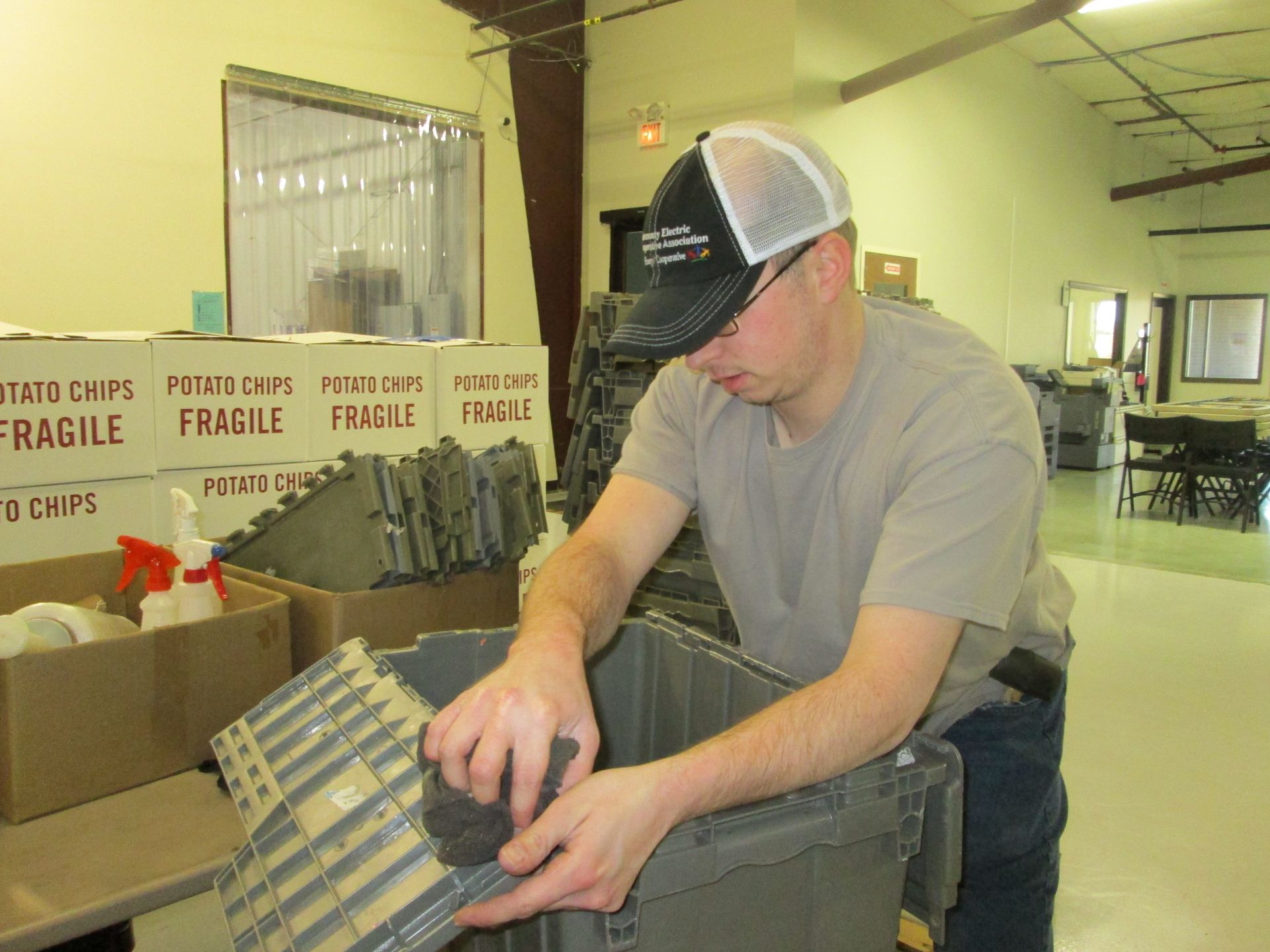Two people reviewing packages, one using a tablet, the other writing. Studio setting with craft supplies.