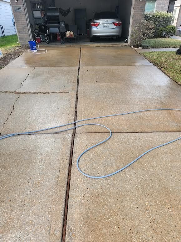 Wet driveway with a blue hose stretched across it, leading to a garage with a car inside.