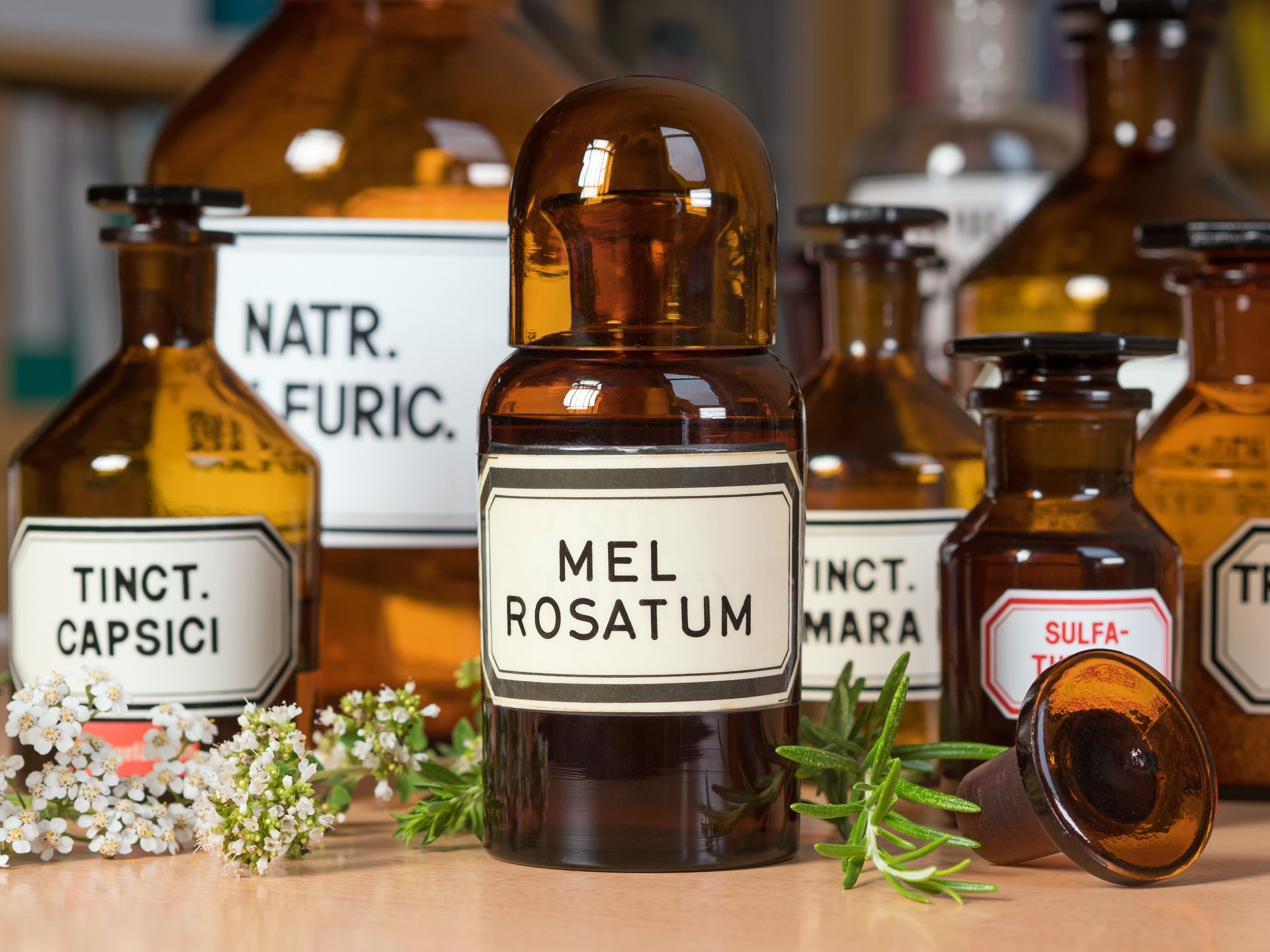 Antike Apothekerflaschen mit weißen Etiketten und braunem Glas, Kräuter vorhanden.