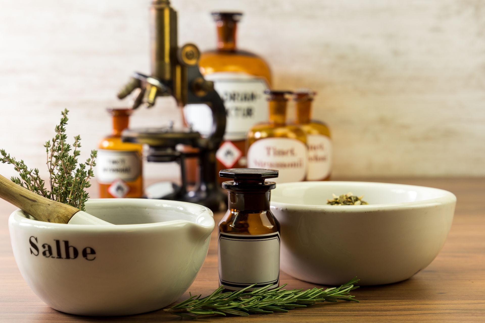 Mörser und Stößel mit Kräutern, Apothekergläsern, einem Mikroskop und Flaschen auf einer Holzoberfläche.