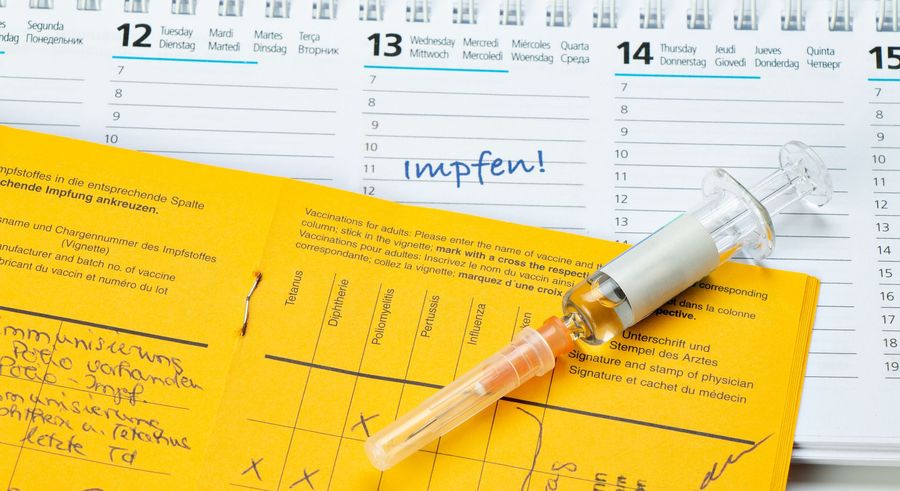 Gelber Impfausweis und Spritze auf einem Kalender mit der Aufschrift „Impfen!“ am 13. Tag.