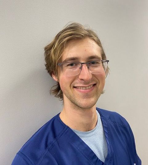 A man, Will Skinner, wearing glasses and a blue scrub is smiling for the camera.