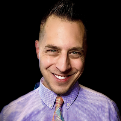 A man, Ian Neuhaus, in a purple shirt and tie is smiling .