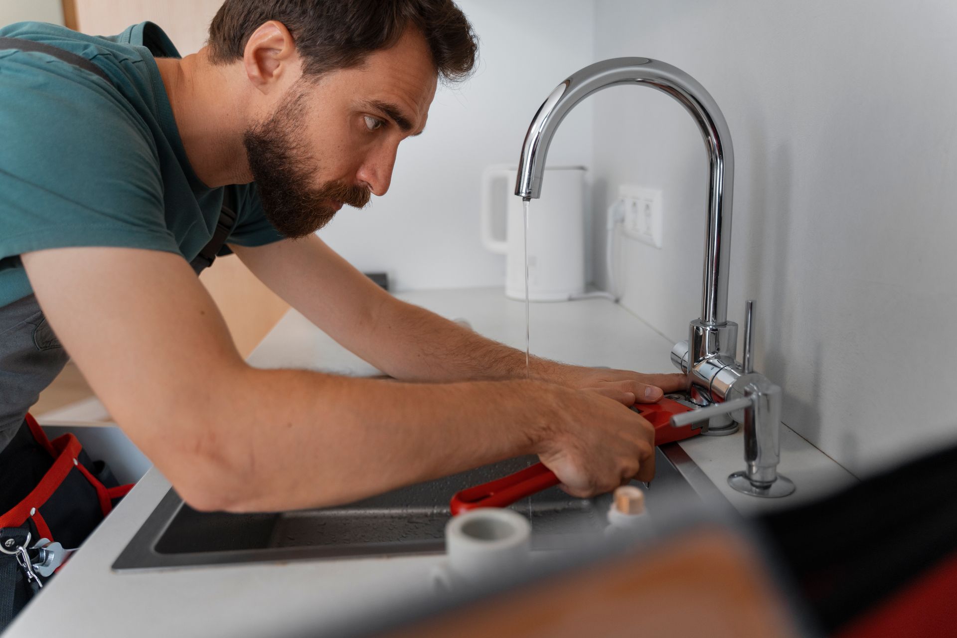 Plumber using pliers to fix a kitchen sink faucet, white counter, focus on hands and fixture.