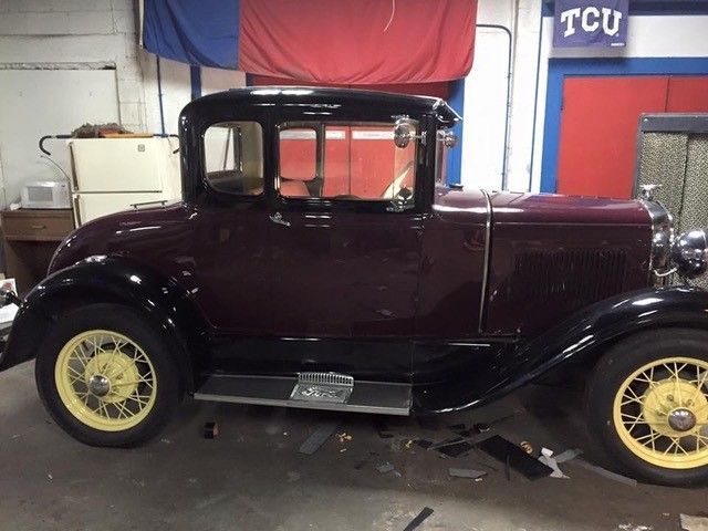 An old car is parked in front of a sign that says tcu