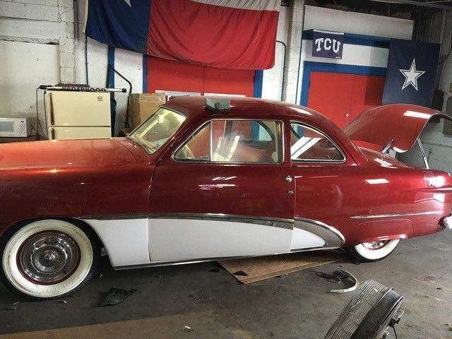 A red car is parked in a garage with the hood up