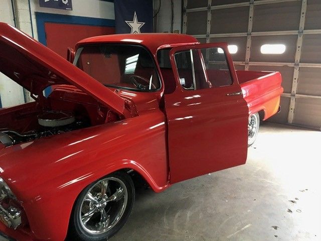 A red truck with the hood up is parked in a garage
