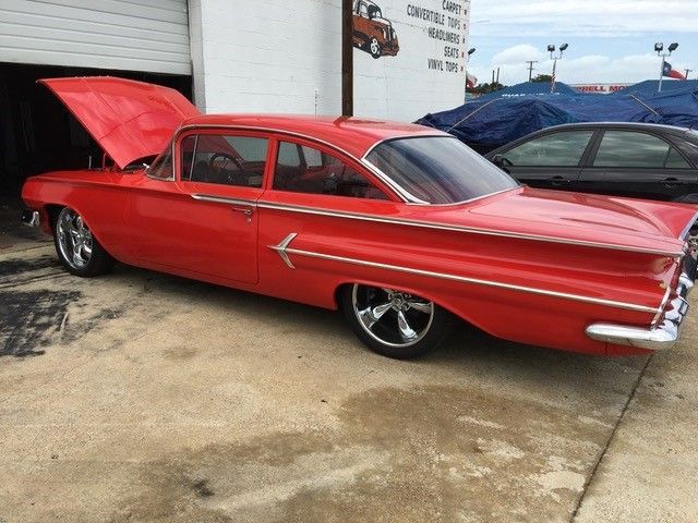 A red car with the hood up is parked in front of a garage