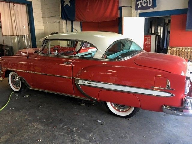 A red car is parked in a garage with a sign that says tcu