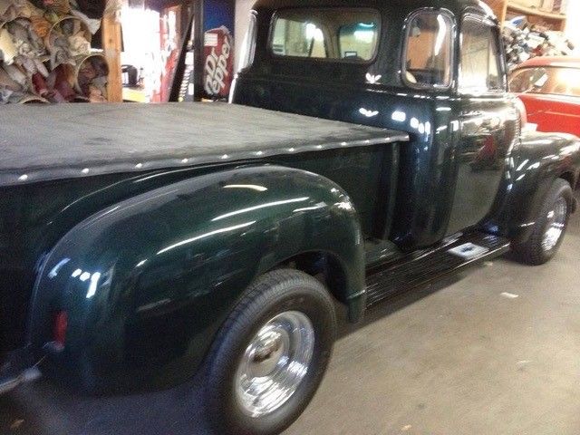 A green truck with a black tonneau cover is parked in a garage