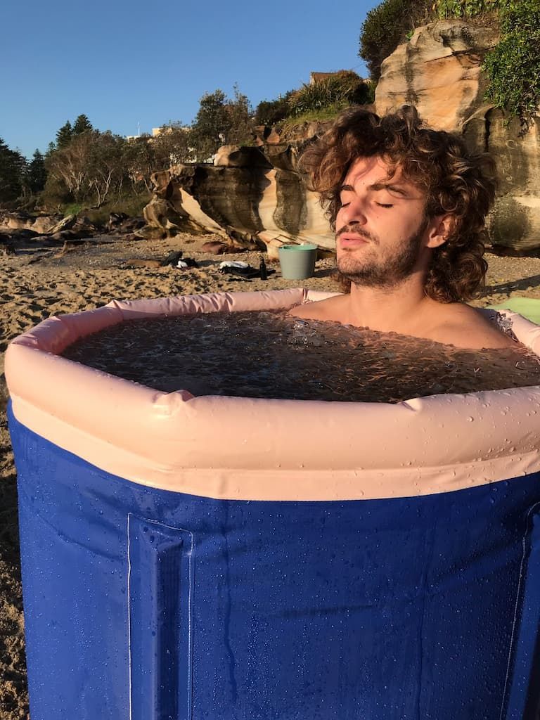 A man is taking a bath in an inflatable tub on the beach.