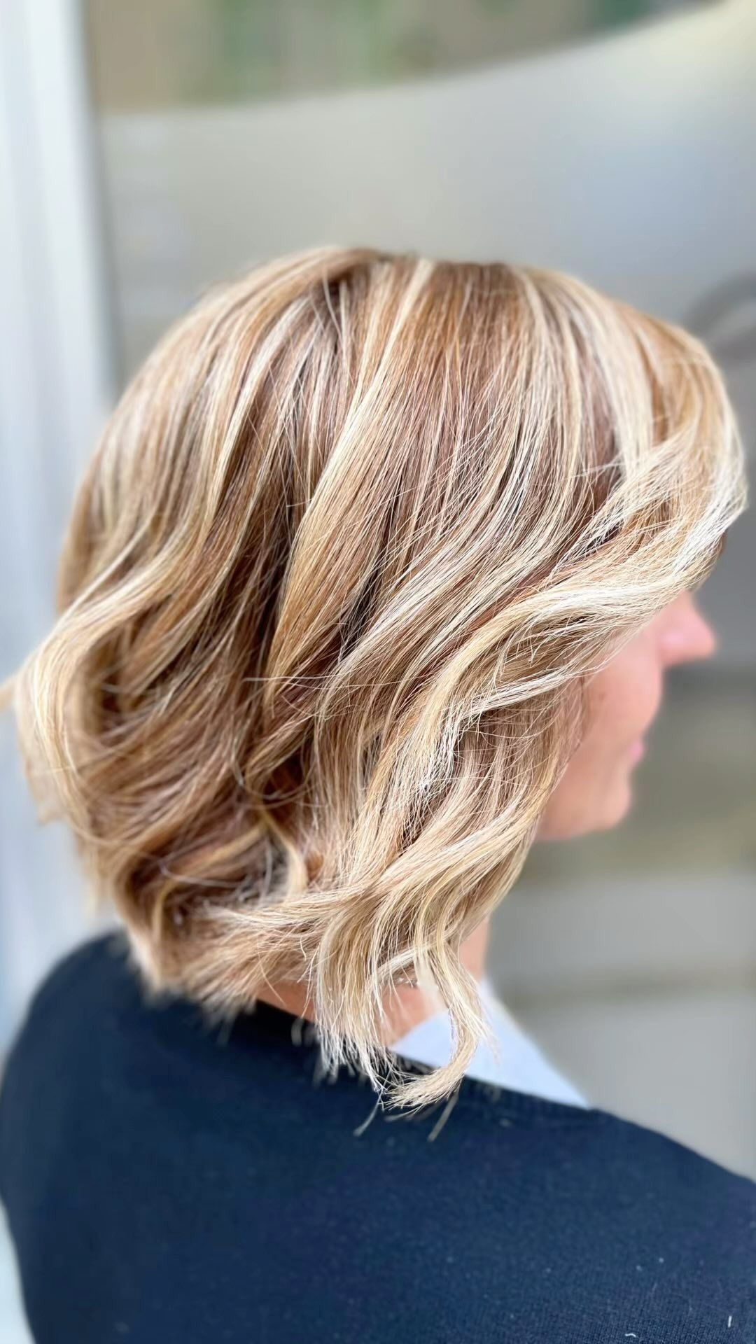 Una donna con i capelli biondi corti indossa un maglione nero.
