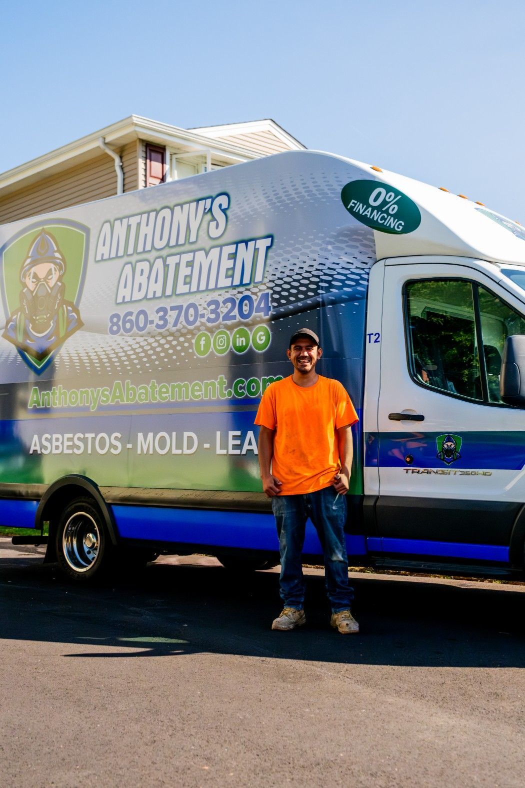 Man in orange shirt standing beside blue mold remediation truck with company branding on a sunny street