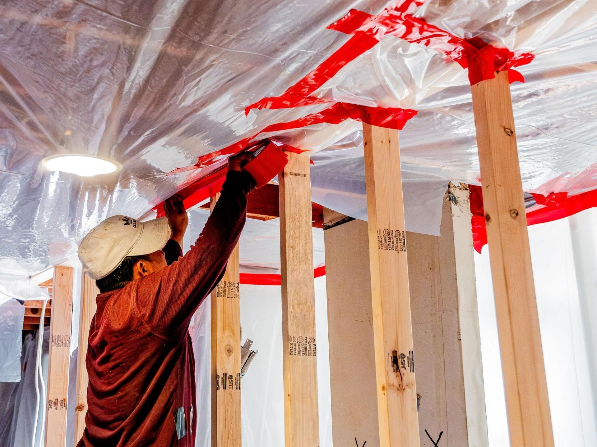 A man is covering a wall of a building with red tape to control asbestos spread
