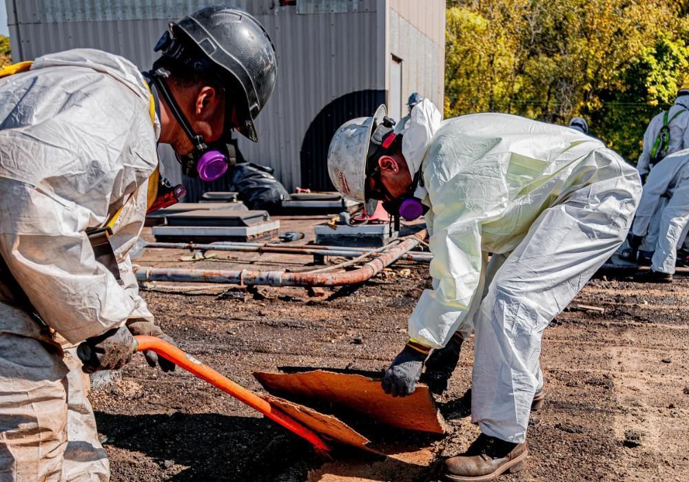 Two men in protective suits are digging up asbestos cement