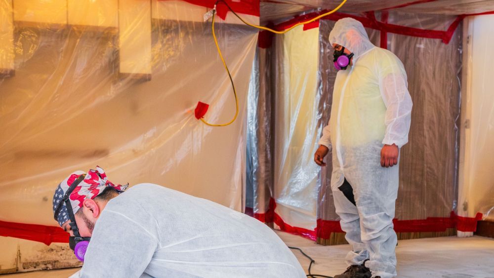 Two men in protective suits removing asbestos tile