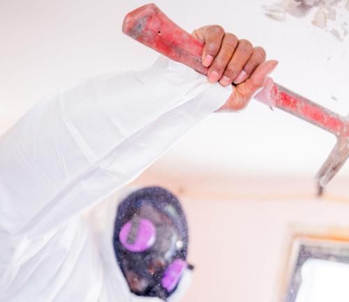 A person wearing a mask demolition a ceiling with a hammer