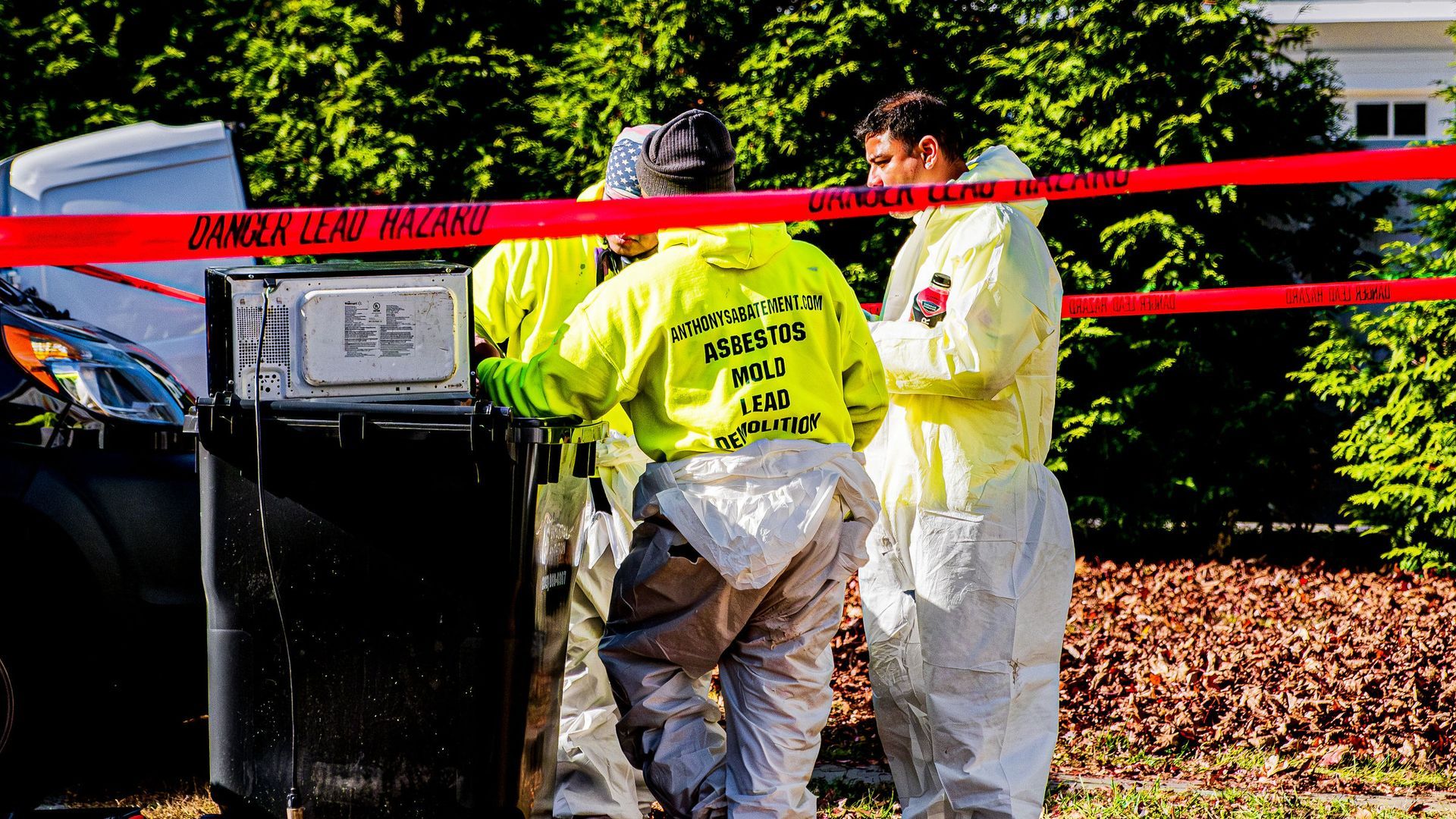 A group of people in protective suits are standing around a trash can.