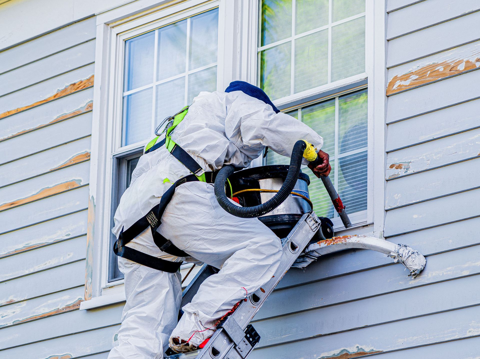 A man is cleaning a window on the side of a house with a vacuum cleaner.