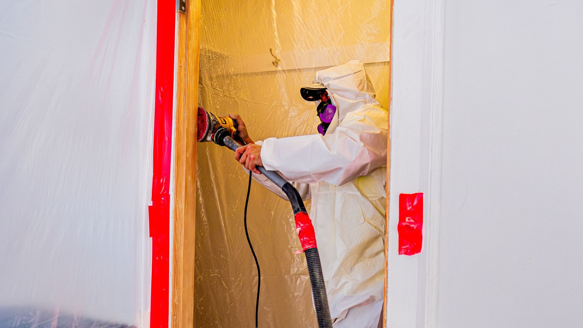 A man in a protective suit is using a vacuum cleaner to clean a wall.