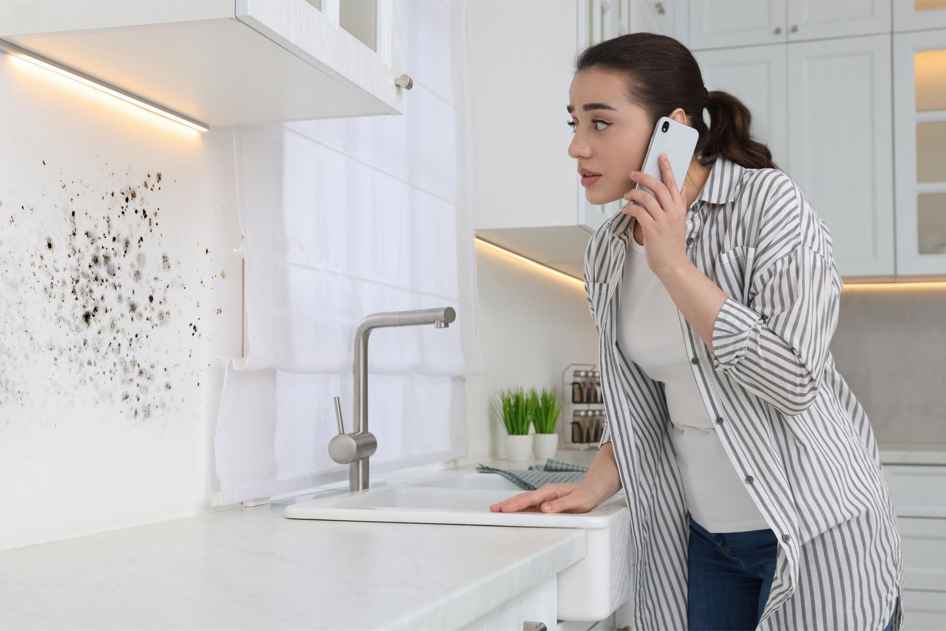 A woman is standing in a kitchen talking on a cell phone about mold 