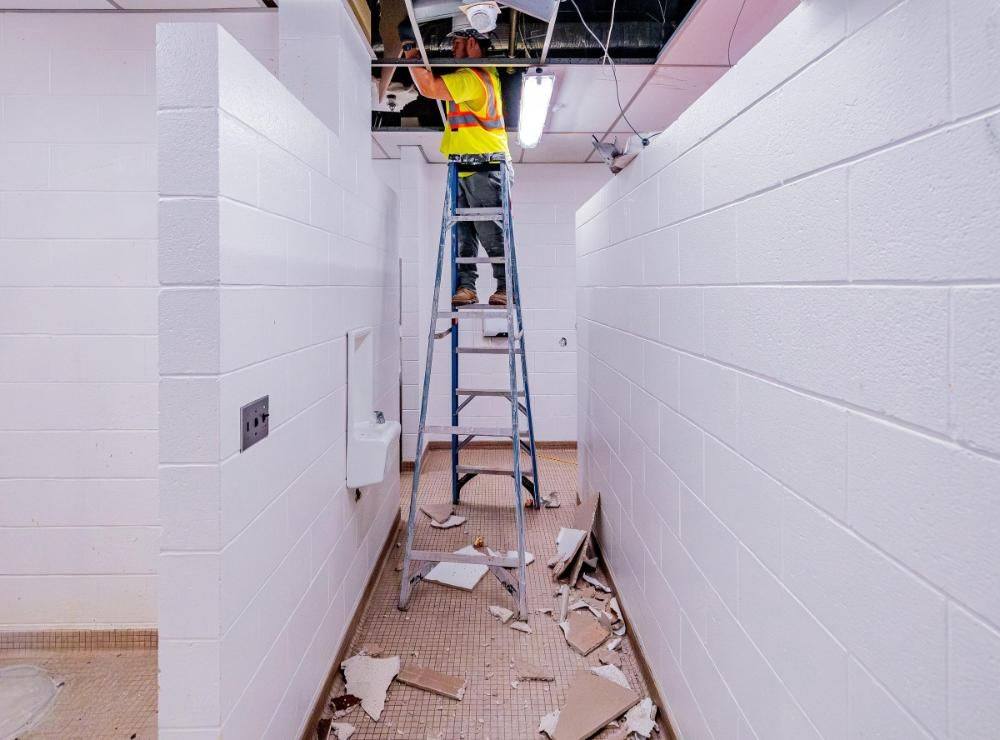 A man is standing on a ladder in a hallway demolition a ceiling