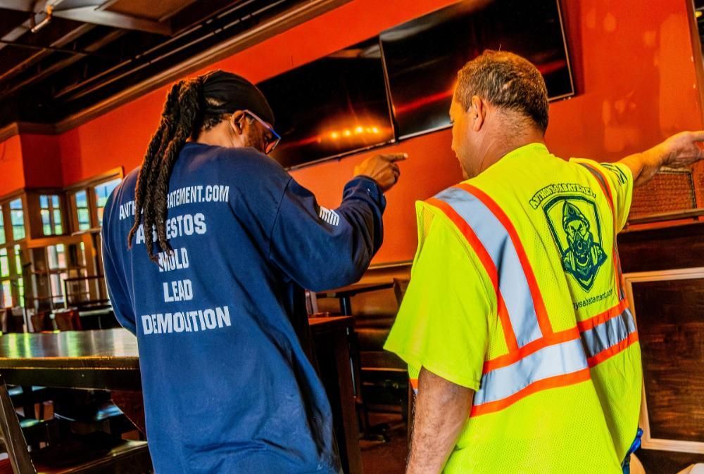 Two men in safety vests are pointing at something in a room.