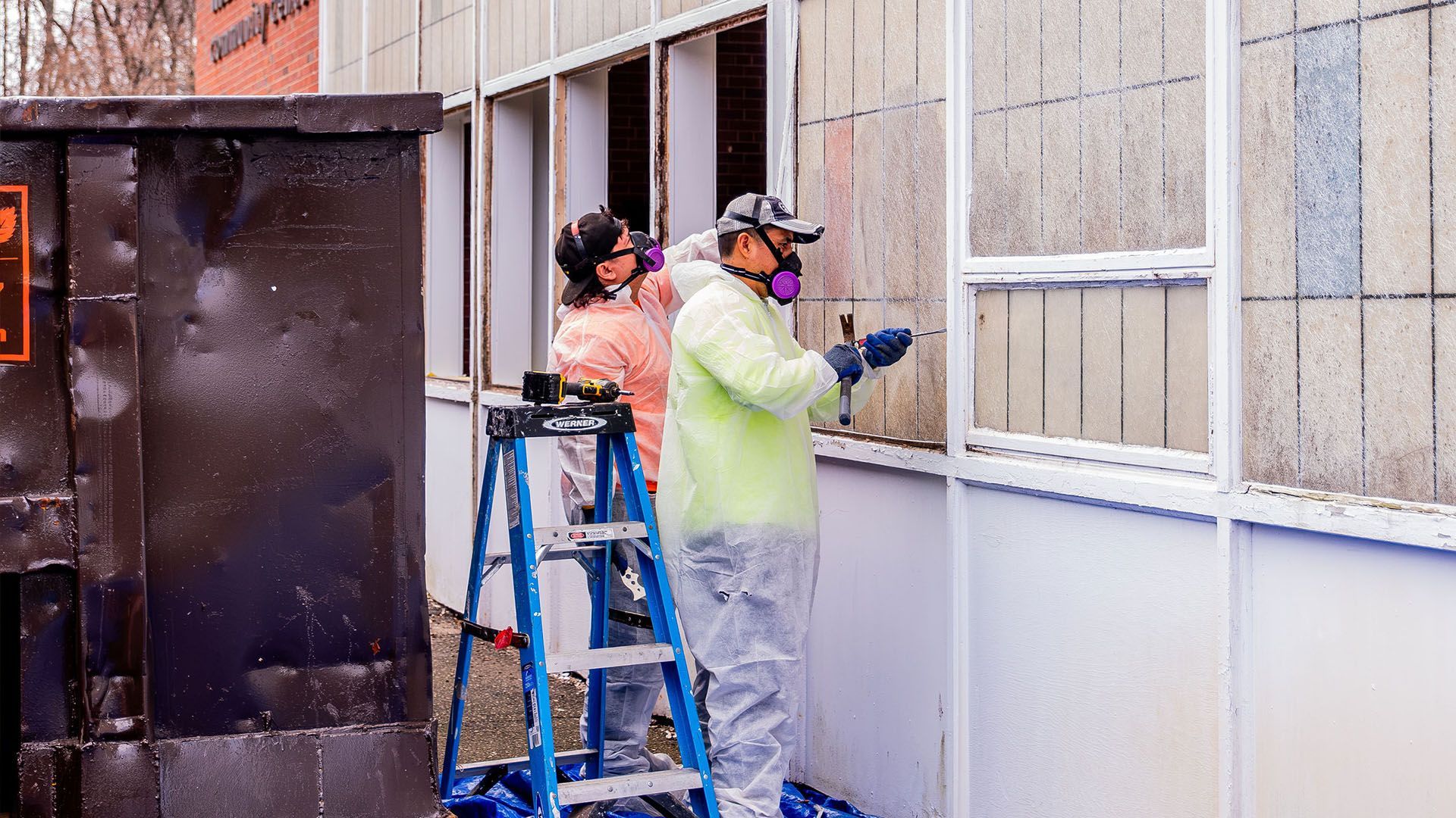 Two men wearing gas masks are working on a building.