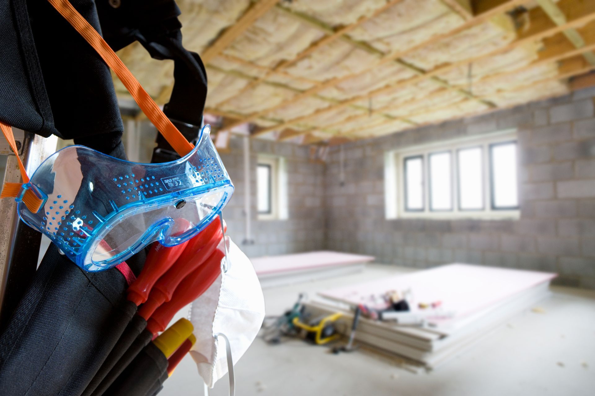 Blue safety goggles on construction gear at a partially built room with insulation and materials on the floor