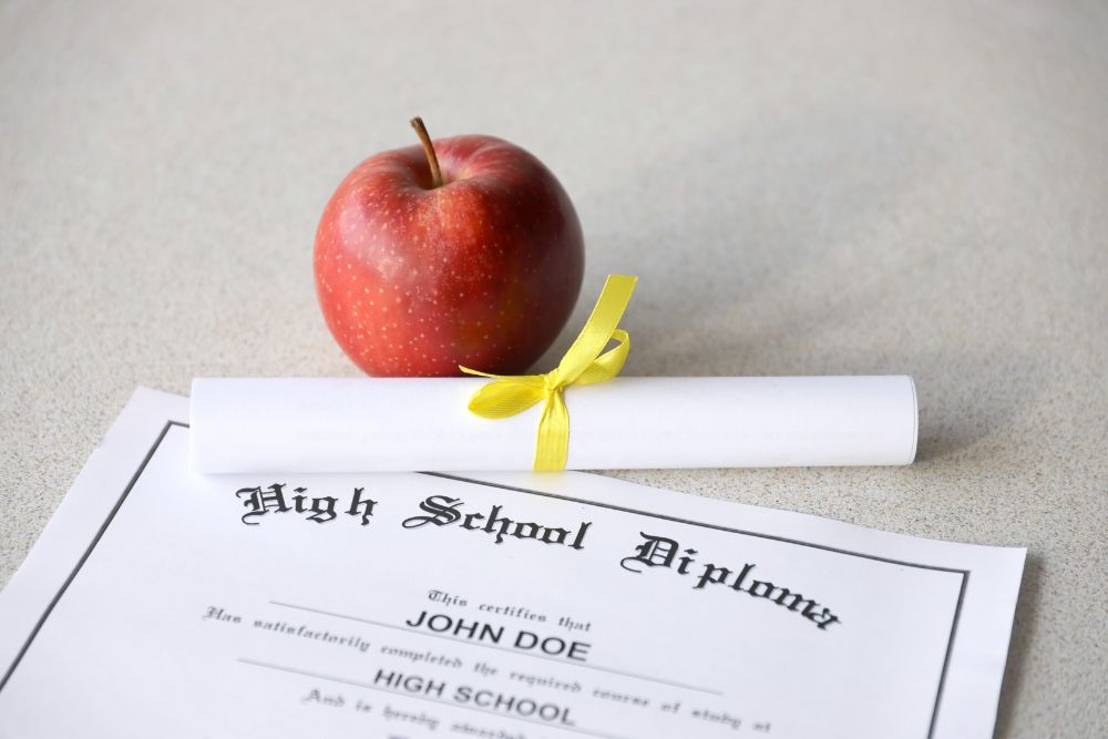 A red apple sits next to a high school diploma