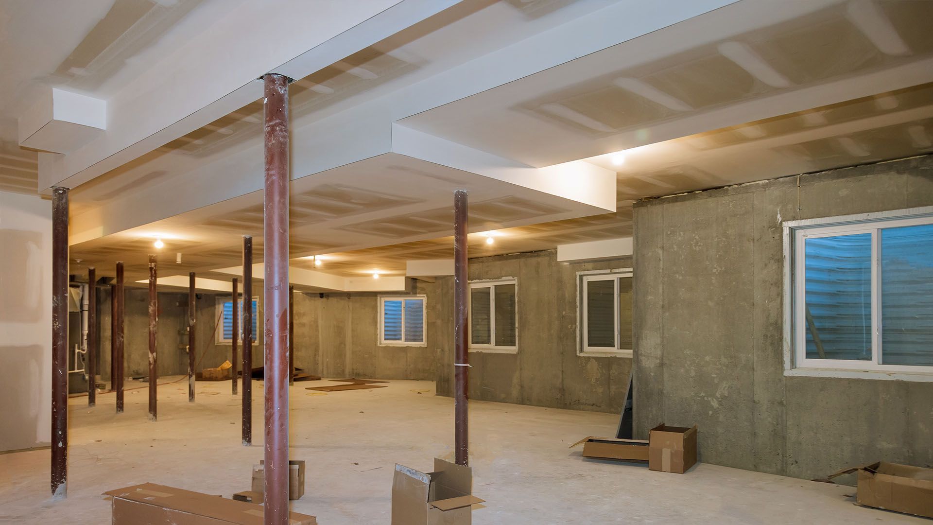 Basement renovation: drywall ceiling, support beams, concrete walls, windows.