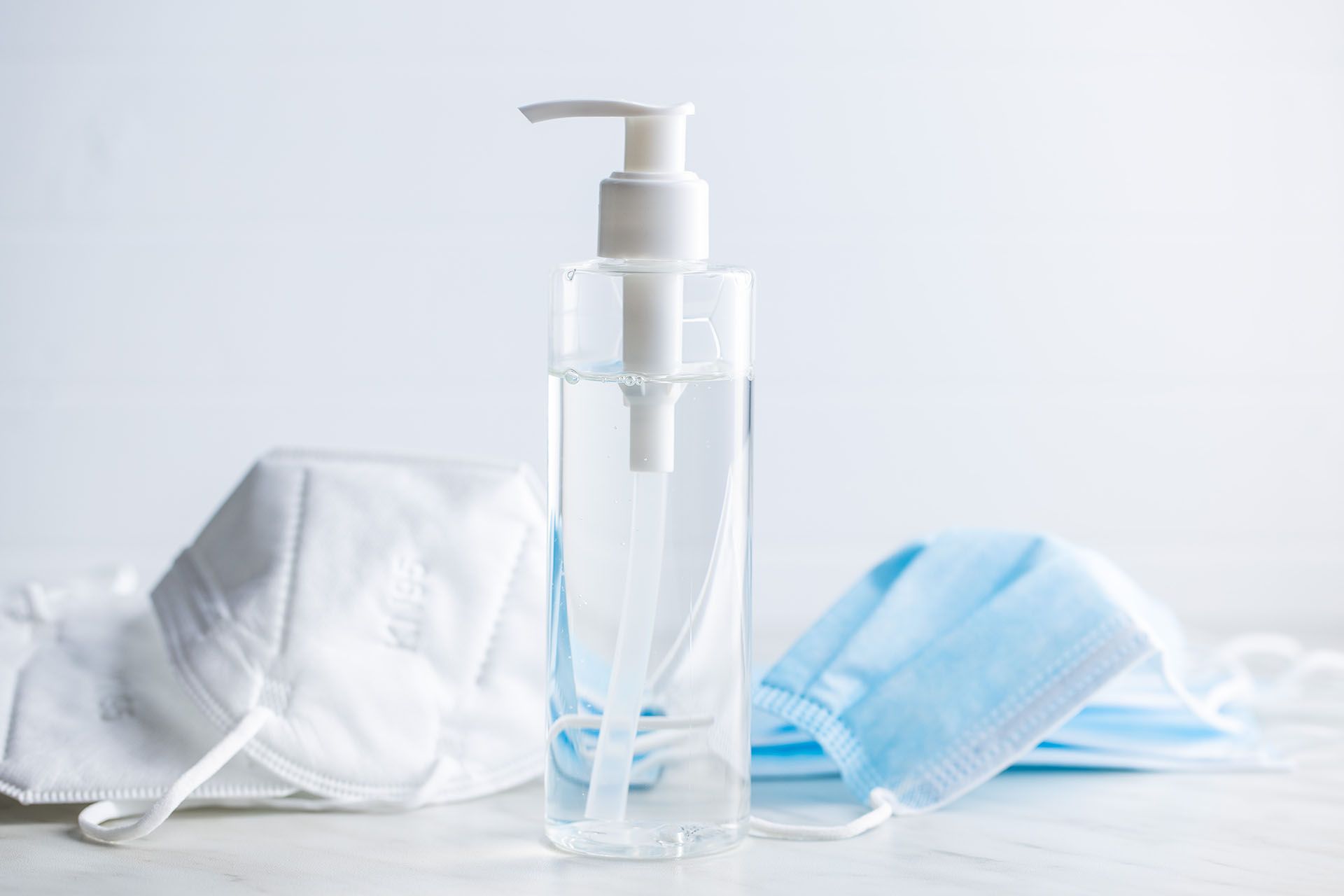 Hand sanitizer dispenser with two face masks on a white surface.