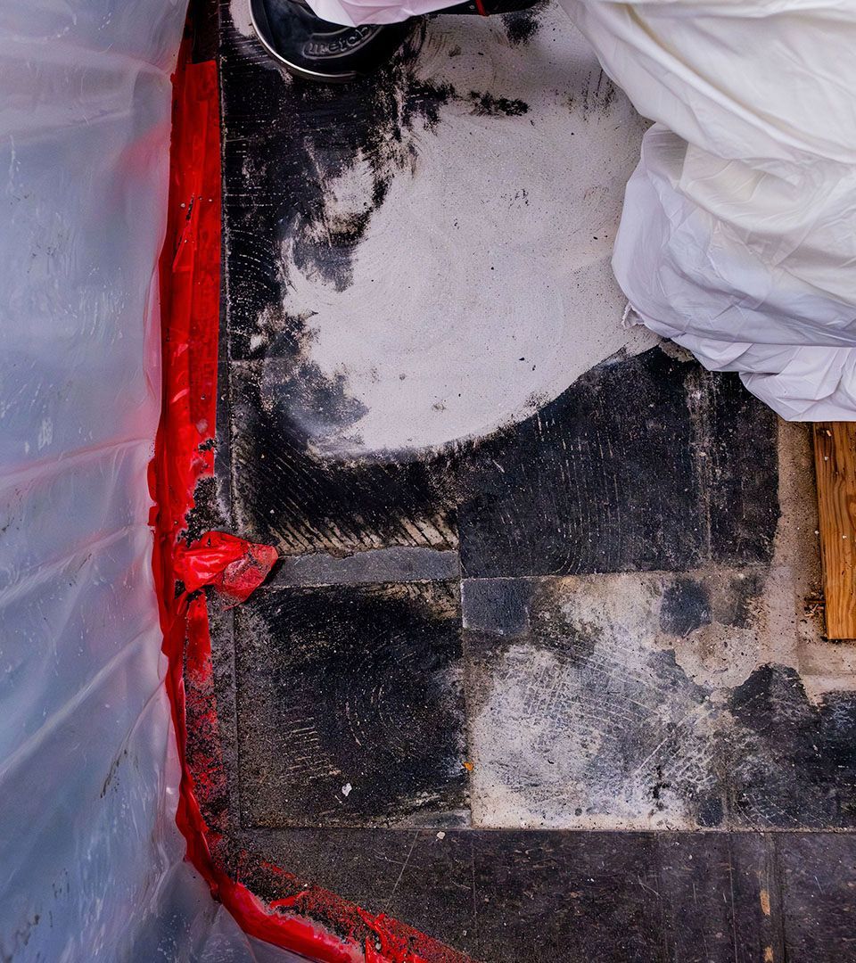 Red sealant along a wall, next to damaged black and white checkered floor. Protective suit visible.