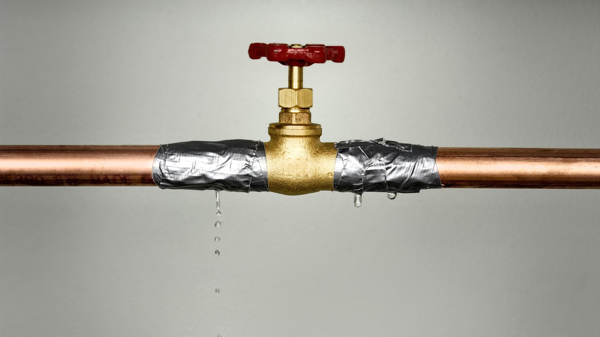 A copper pipe with a red valve is leaking water.