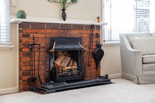 Classic brick fireplace with vintage cast-iron tools, ready for use, situated in a cozy living room with soft furnishings.