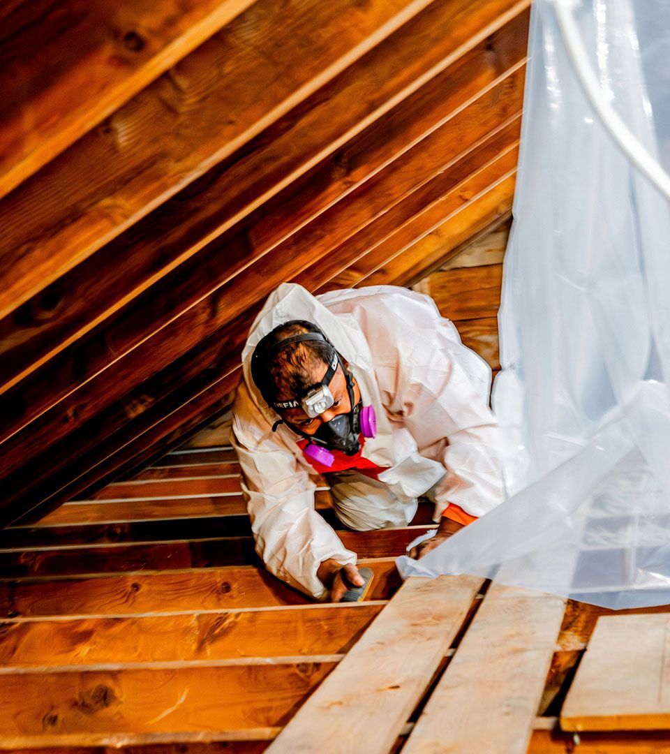 Person in protective suit working in an attic, dust mask, wood planks, light.