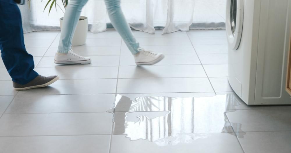 A man and a woman are walking on a tiled floor next to a washing machine.