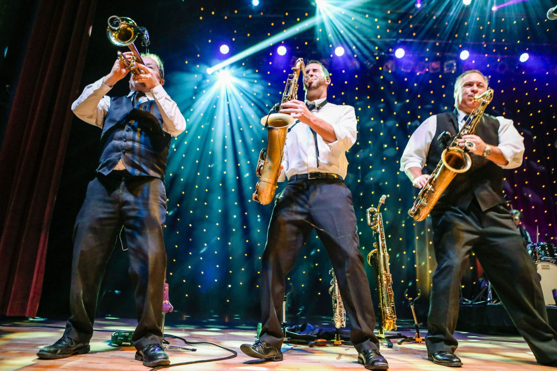 three men are playing saxophones and trumpets on a stage .