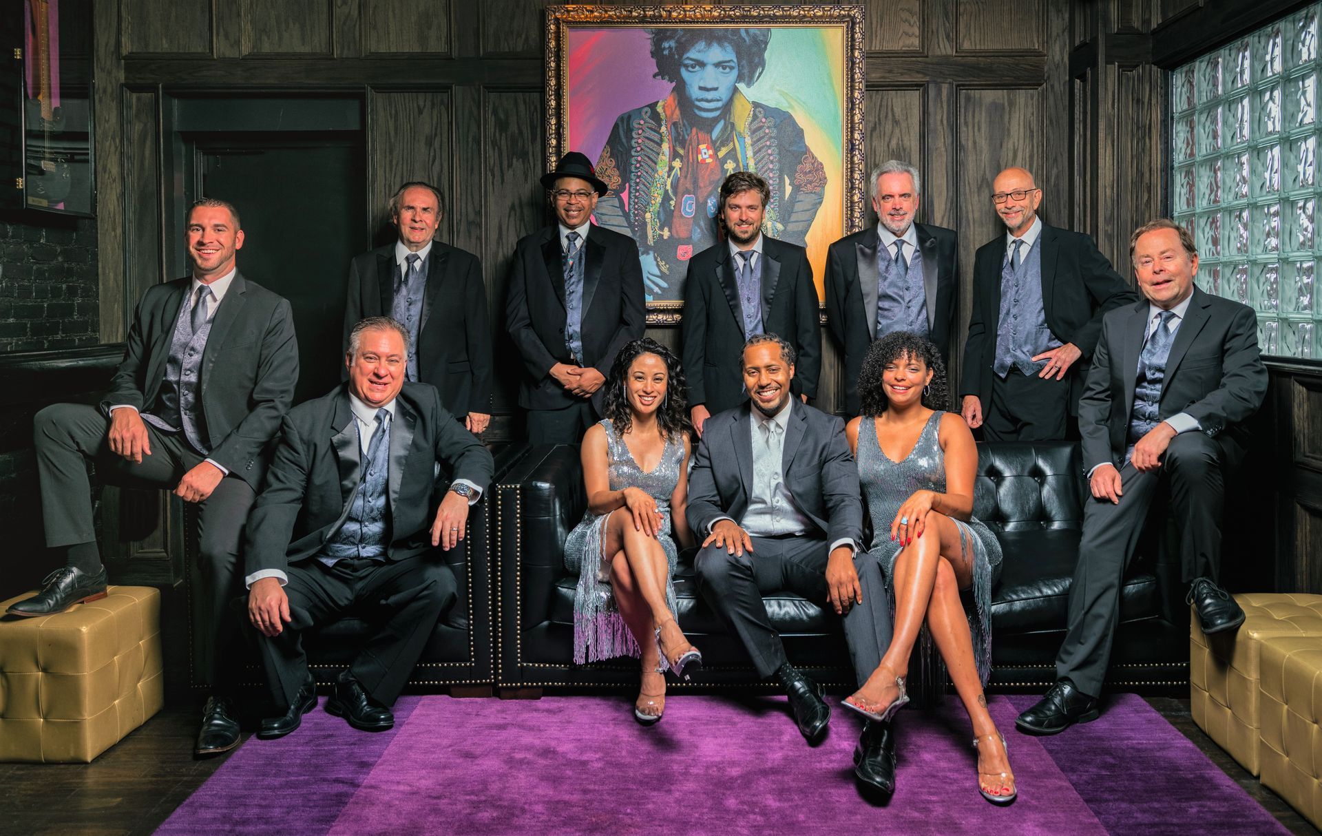 The ultimate experience: Mainstreet Soul full band posing in front of Jimi Hendrix's colorful painting wearing black and silver.