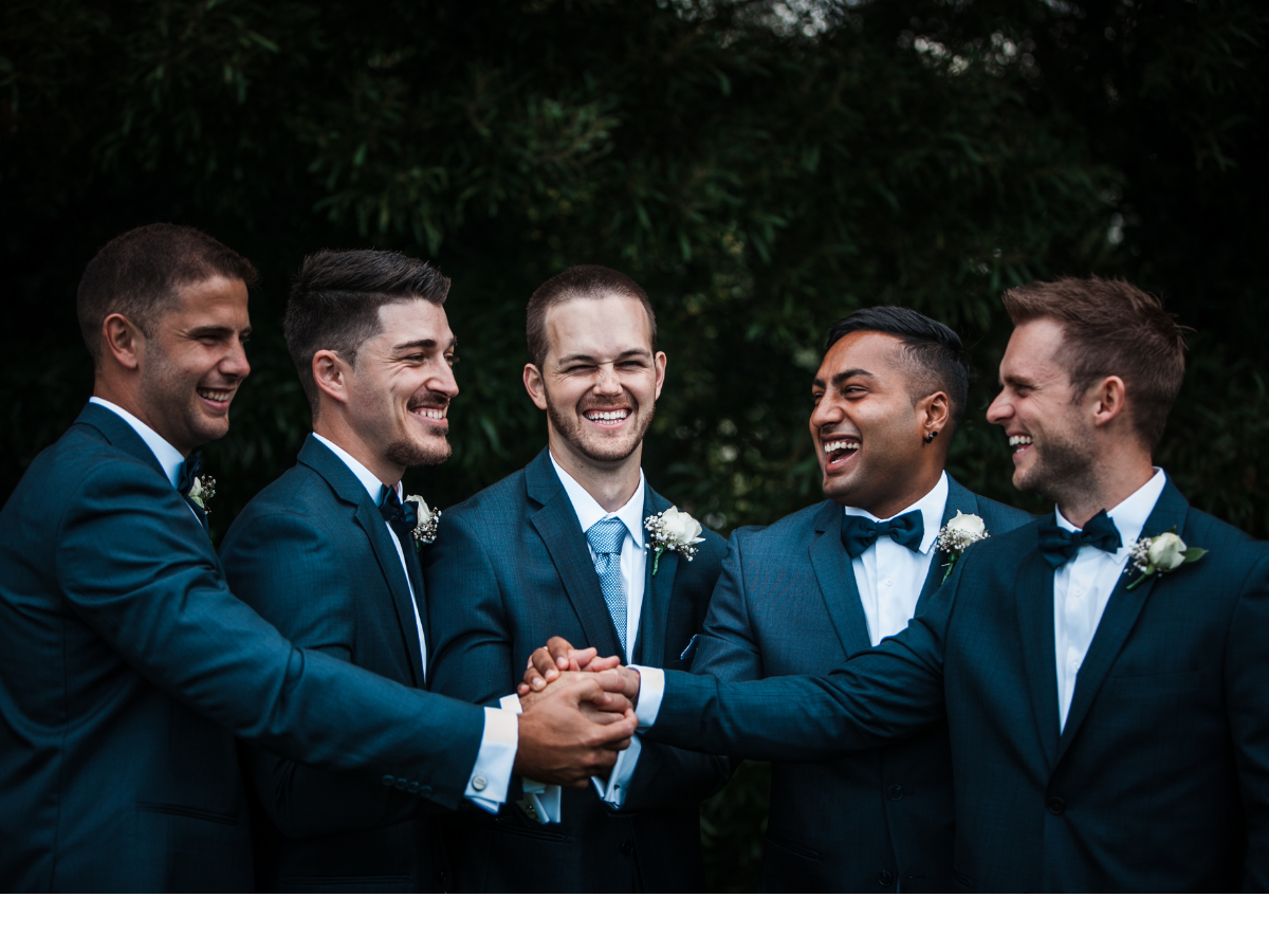 a group of men in suits are holding hands and smiling at a wedding