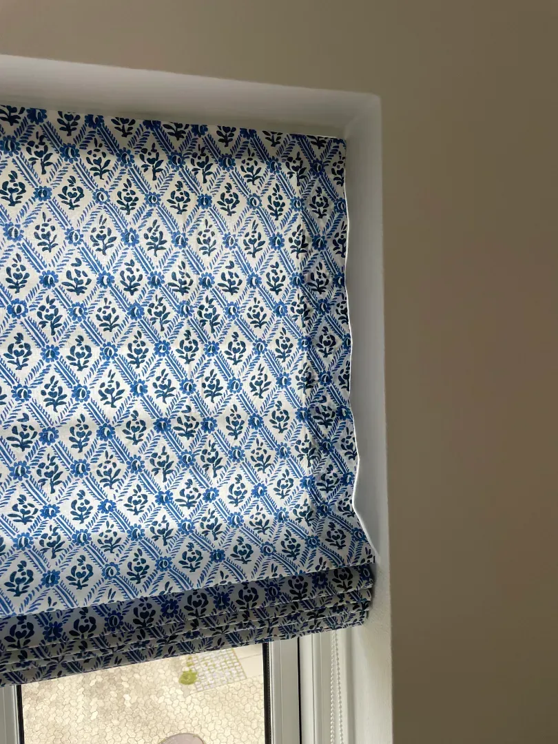 Beige rullegardiner, der delvist dækker et vindue, set indefra en bygning.