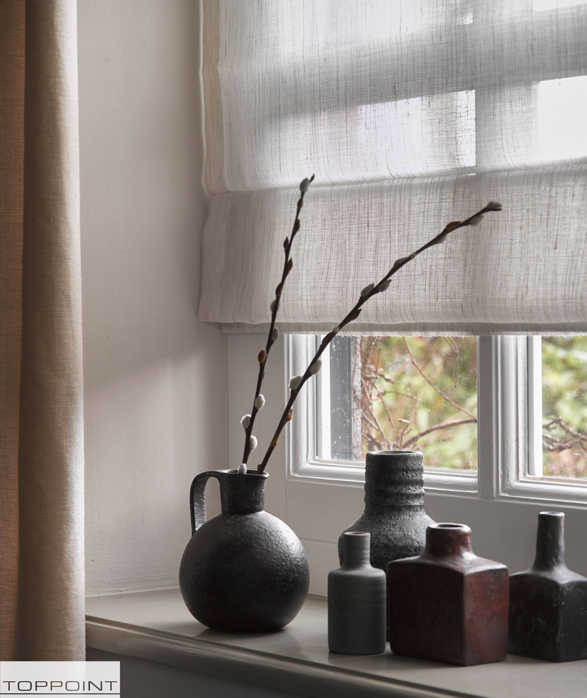 Brune gardiner med metalmaljer hænger foran en væg; aircondition ovenover.